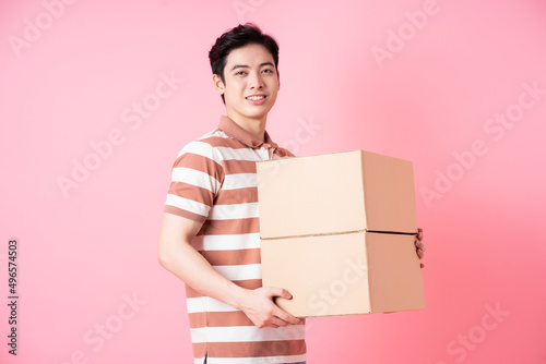 Image of young Asian man holding cardboard on pink background © Timeimage