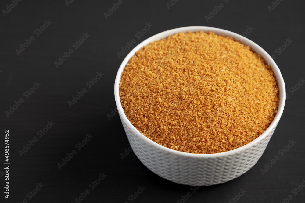 Brown Demerara Sugar in a Bowl on a black background, side view. Copy space. Brown Demerara Sugar in a Bowl on a black background, side view. Copy space.