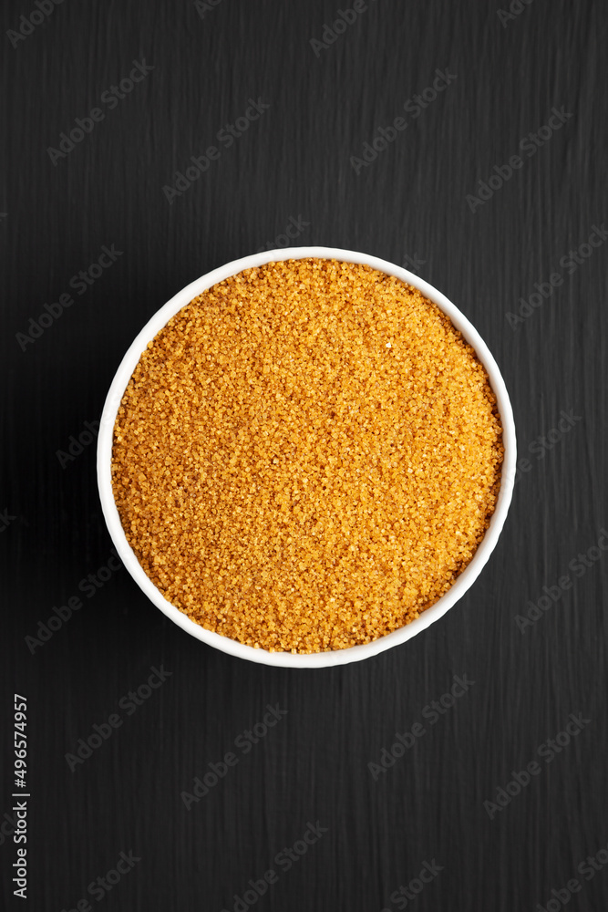 Brown Demerara Sugar in a Bowl on a black background, top view. Flat lay, overhead, from above. Brown Demerara Sugar in a Bowl on a black background, top view. Flat lay, overhead, from above.