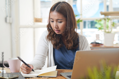 Asian people study online course via internet. Young girl watching business lesson from laptop computer and note lecture to notebook at home.