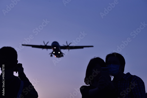 Three people looking up at flying airplane against blue sky during dusk 