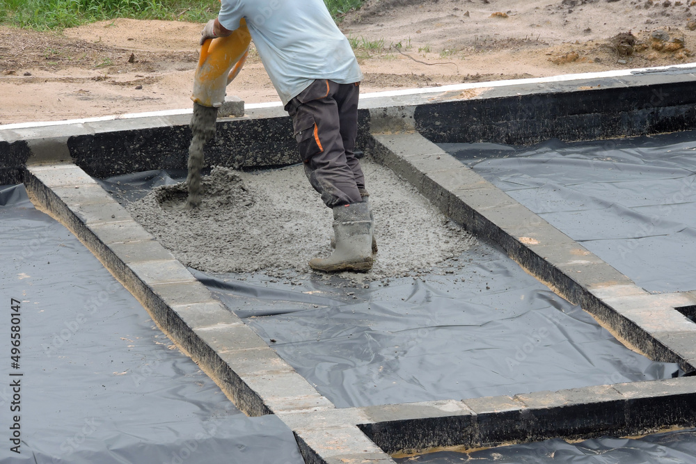 A building worker pouring a concrete slab foundation using a hose of a concrete pump truck A building worker pouring a concrete slab foundation using a hose of a concrete pump truck