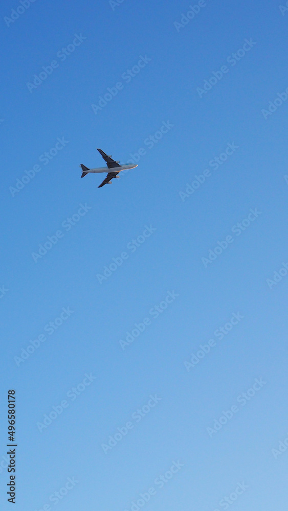 The big four-engine transport airplane is flying far away in the blue sky. Plane in the air. International air freight. Vertical stories The big four-engine transport airplane is flying far away in the blue sky. Plane in the air. International air freight. Vertical stories