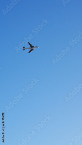 The big four-engine transport airplane is flying far away in the blue sky. Plane in the air. International air freight. Vertical stories