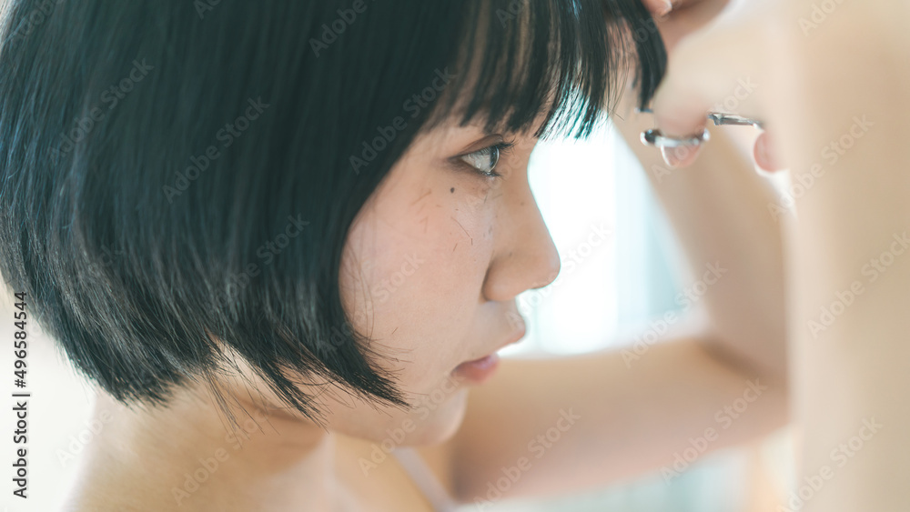 Fototapeta premium Young adult authentic asian woman self cutting bangs haircut with scissors