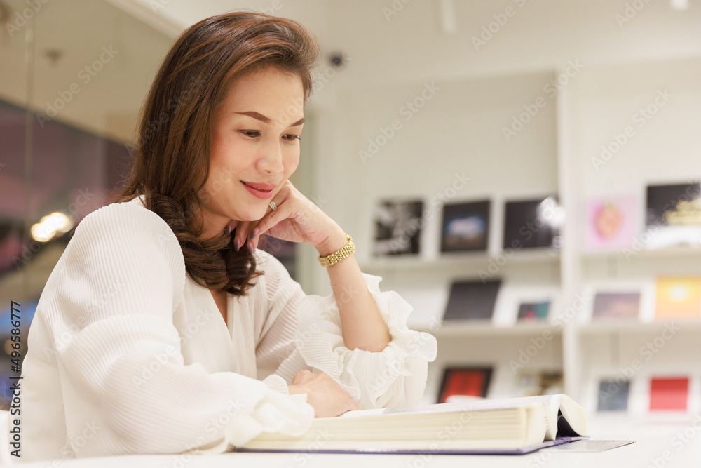 Portrait of Asain pretty cheerful female cozy sitting and reading book in library and leaning on glass wall with happy, focus and concentrate on contents Portrait of Asain pretty cheerful female cozy sitting and reading book in library and leaning on glass wall with happy, focus and concentrate on contents