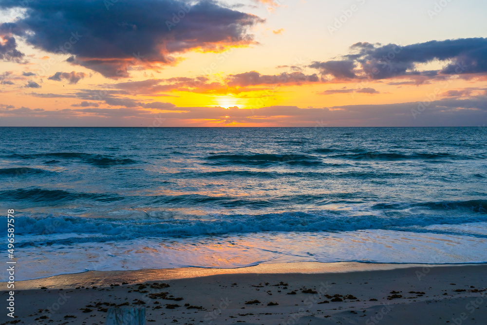 Obraz premium Sunrise over the Atlantic Ocean in the early morning in Florida. The sun illuminates the sky with a golden color in the clouds and is reflected on the dark waters of the ocean.