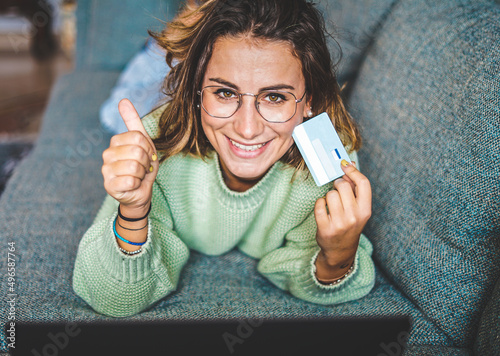 Attractive girl spending his time on shopping online - Young girl relaxing on couch while buying clothes with his credit card photo