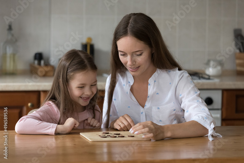 Happy mom and little daughter girl engaged in learning board game. Mother teaching kid to play checker draughts, training tactical and logical skills. Parenthood family leisure time concept