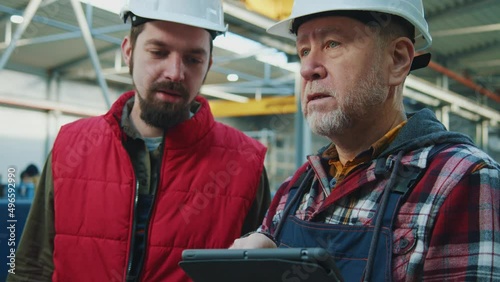 Close up young and elder engineers men heavy industrial workers with helmet using a digital tablet in factory. Checks production processes. Inspector in warehouse. photo