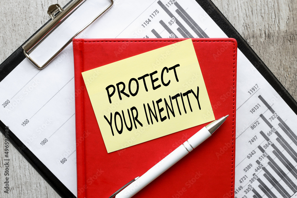 Protect Your Identity. text on yellow sticky note on red notepad on financial charts Protect Your Identity. text on yellow sticky note on red notepad on financial charts