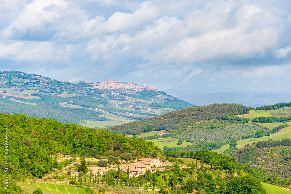 Green landscape in Tuscany, Italy. Unique view of medieval village and stone tower perched on rock cliff against dramatic sky.