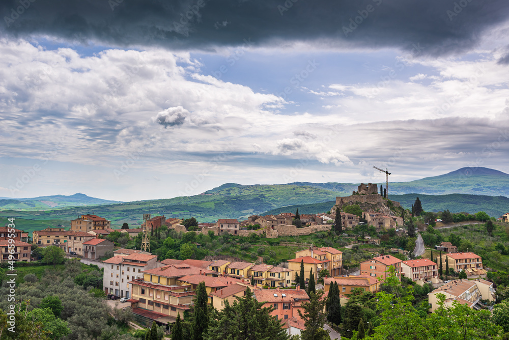Green landscape in Tuscany, Italy. Unique view of medieval village and stone tower perched on rock cliff against dramatic sky.