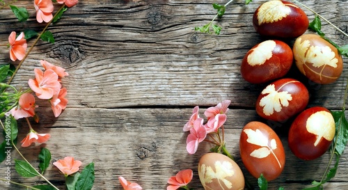 Easter background. Eggs are laid out in a circle with sprigs of plants and geranium flowers on a wooden vintage background.Place for your text.