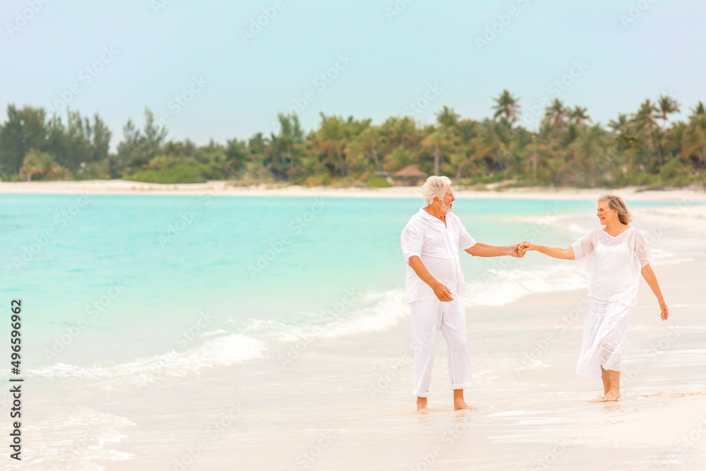 Senior Caucasian couple in white clothes dancing on a tropical beach vacation