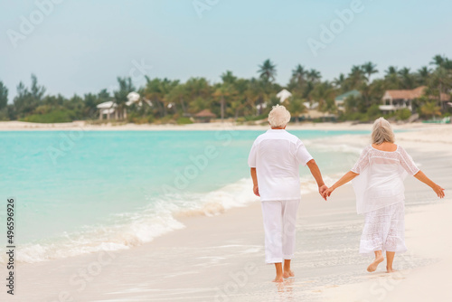 Barefoot Caucasian senior couple in white clothes on a travel resort beach