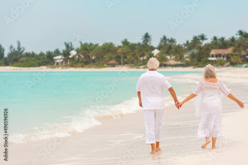 Fototapeta Naklejka Na Ścianę i Meble -  Barefoot Caucasian senior couple in white clothes on a travel resort beach