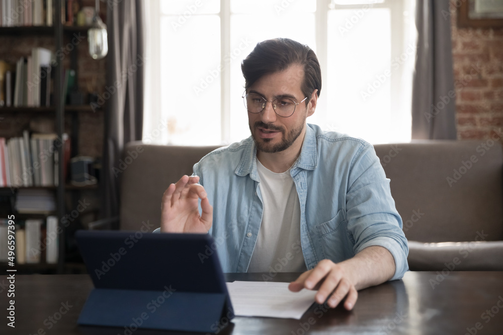 Busy serious businessman in casual talking to client on video call, giving consultation, negotiating on deal, discussing project with partner, using tablet computer at work table Busy serious businessman in casual talking to client on video call, giving consultation, negotiating on deal, discussing project with partner, using tablet computer at work table