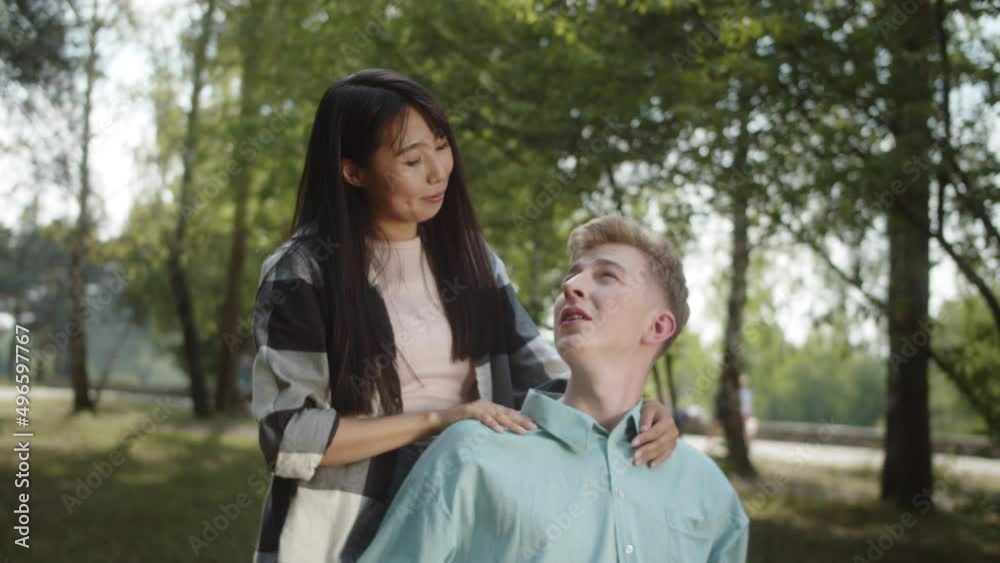 A pretty young asian girl is stroking her boyfriend's shoulders, they are talking together in the public park and looking to each other, slow motion A pretty young asian girl is stroking her boyfriend's shoulders, they are talking together in the public park and looking to each other, slow motion
