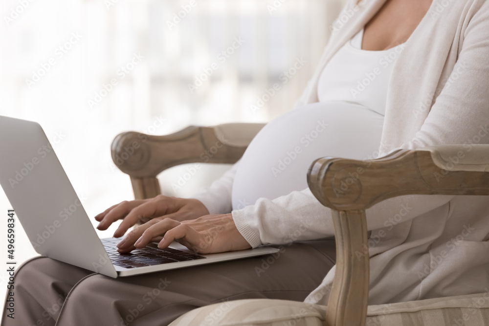 Naklejka premium Pregnant freelance distance employee woman working from home. Hands typing on laptop keyboards at big belly close up. Expecting woman using laptop for online healthcare consulting chat. Cropped shot