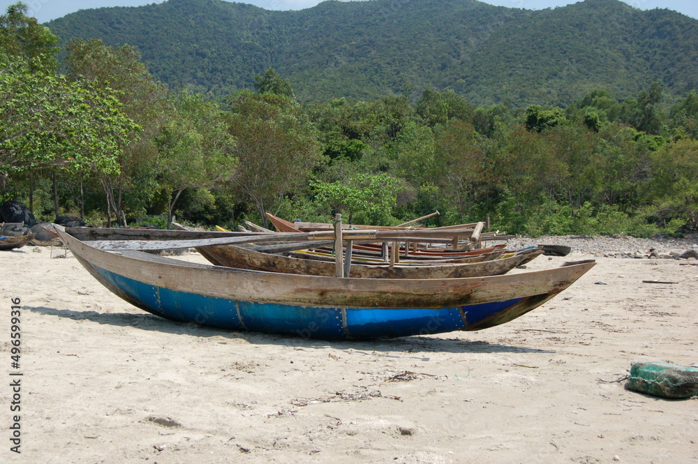 Small wooden fishing boats with paddles on a sandy beach in Vietnam.