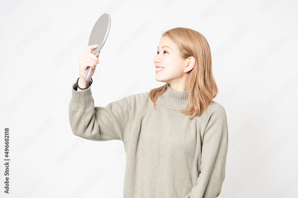 白い背景の前に立って鏡で顔を見る若い女性 白い背景の前に立って鏡で顔を見る若い女性