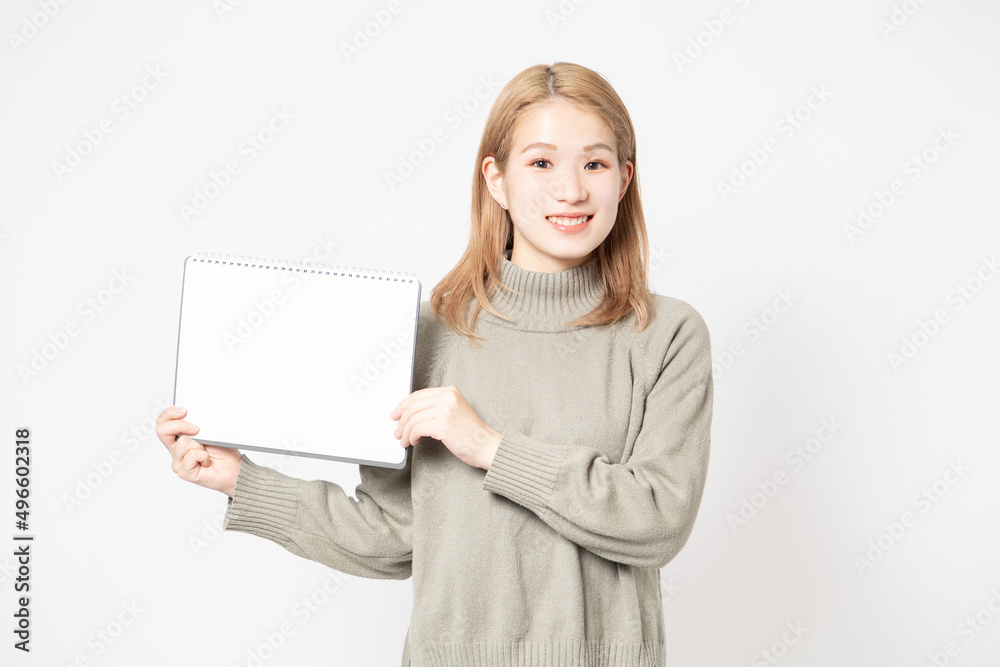 白い背景の前に立って小さいスケッチブックを見せている若い女性 白い背景の前に立って小さいスケッチブックを見せている若い女性