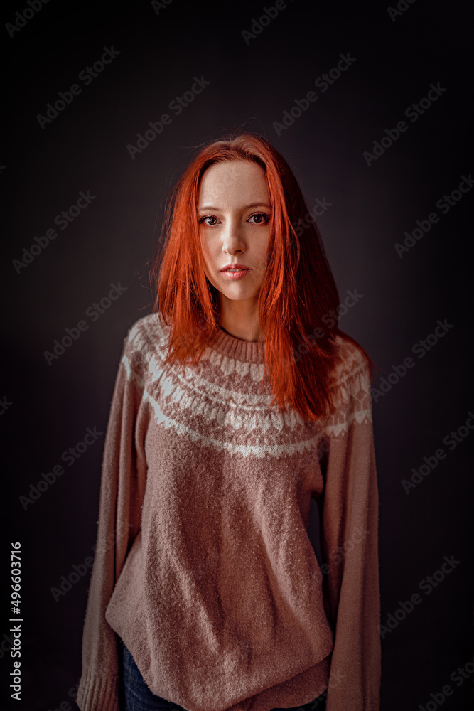 A beautiful slender model girl with fiery red hair, in modest clothes (a warm knitted wrinkled oversize sweater and blue jeans) poses in front of the camera on a black background A beautiful slender model girl with fiery red hair, in modest clothes (a warm knitted wrinkled oversize sweater and blue jeans) poses in front of the camera on a black background