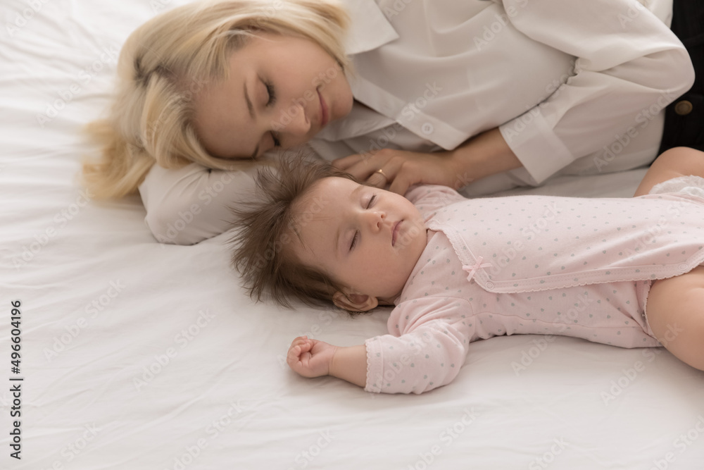 Calm tired new mom and beautiful infant sleeping together, lying in bed on white linen sheet, relaxing in bedroom, taking break, pause. Young mother relaxing near sleepy baby at home. Motherhood Calm tired new mom and beautiful infant sleeping together, lying in bed on white linen sheet, relaxing in bedroom, taking break, pause. Young mother relaxing near sleepy baby at home. Motherhood