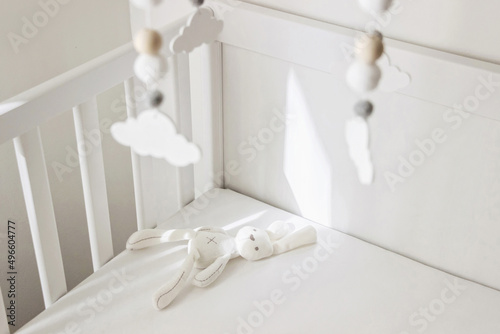 white crib with soft toy and cute cloud mobile in nursery room