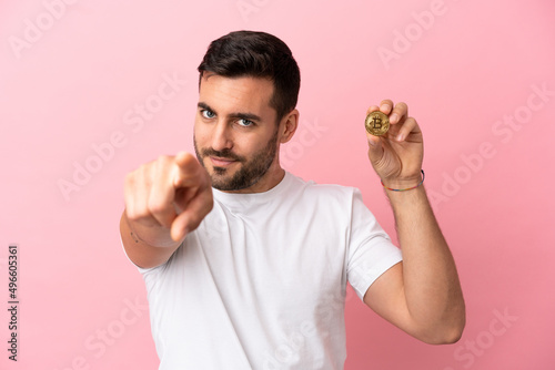 Young man holding a Bitcoin isolated on pink background pointing front with happy expression © luismolinero
