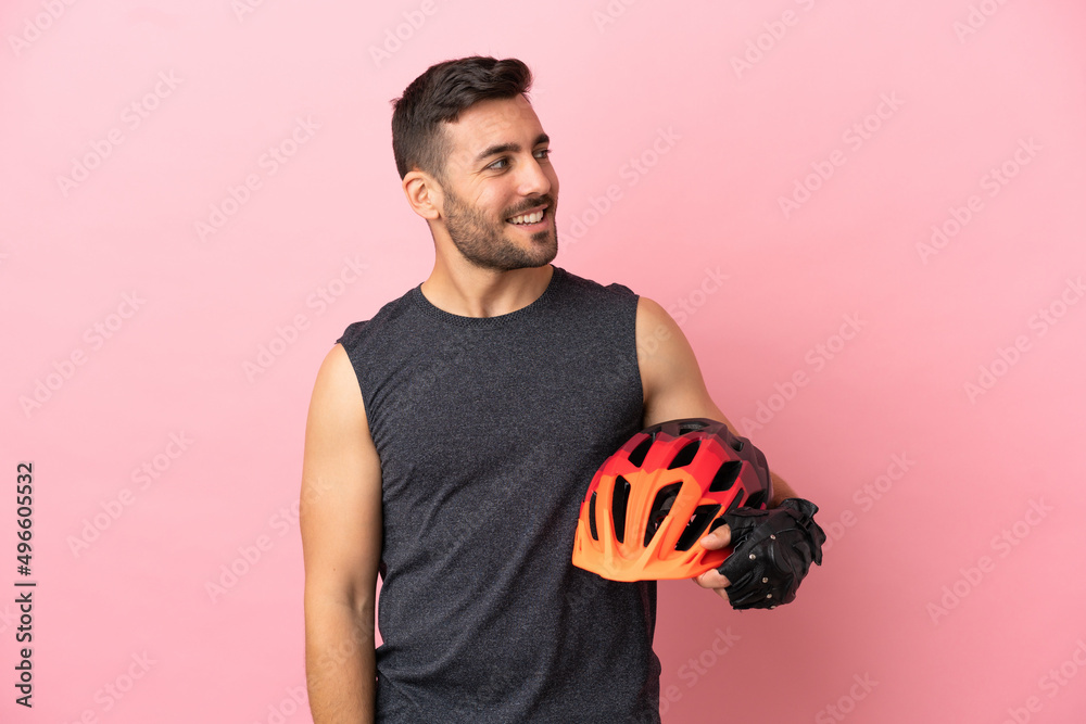 Young cyclist man isolated on pink background looking to the side and smiling - obrazy, fototapety, plakaty 