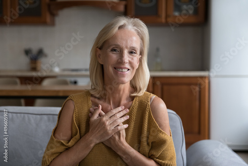 Картината върху платно Happy thankful mature 50s lady posing on home couch, applying hands to chest, heart in gratitude gesture, smiling, expressing hope, love, appreciation, making wish