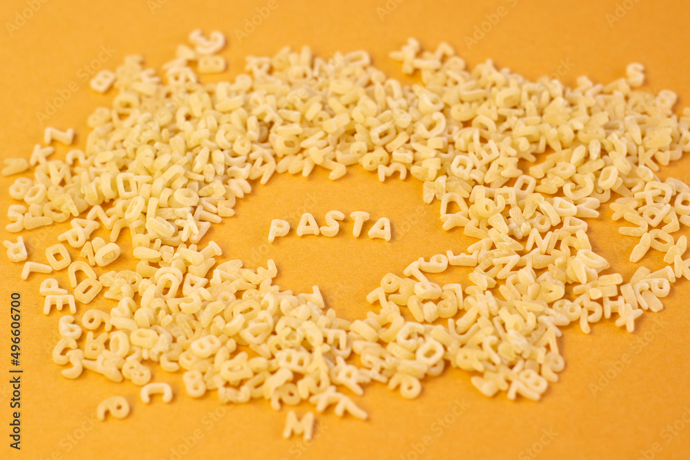 Obraz premium Whole grain dark pasta letters on dark yellow textured background with selected focus