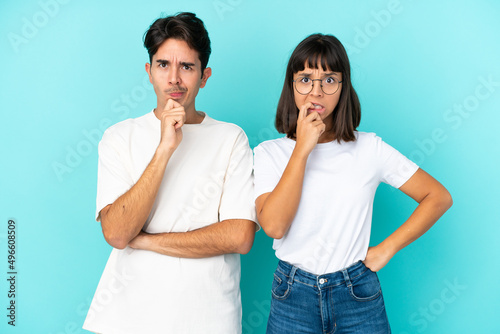 Young mixed race couple isolated on blue background having doubts while looking up