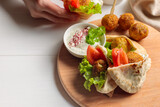 Mini pita with falafel and vegetable salad in sauce. A hand with pita in the background.