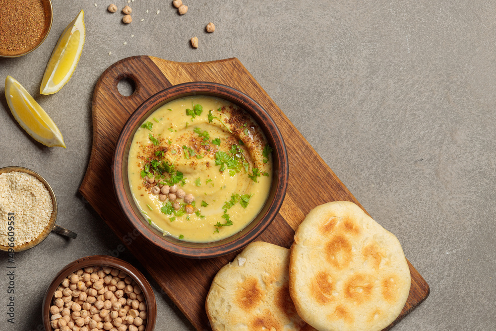 Hummus or fava in a bowl on a wooden board with pita and lemon slices. Top view on a gray background, horizontal