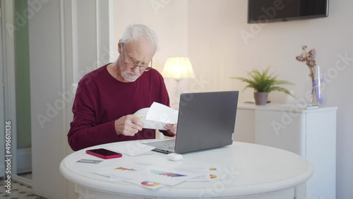  An elderly man pays taxes via the Internet. He scratches his head thoughtfully and examines bills