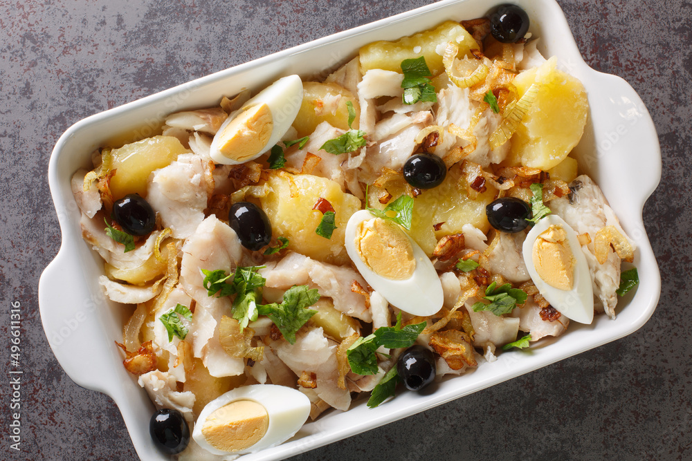 Portuguese Bacalhau a Gomes de Sa salted cod baked with potatoes, onions served with eggs and olives close-up in a baking dish on the table. horizontal top view from above