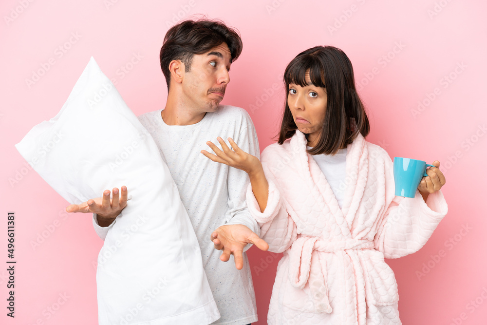 Young couple in pajamas isolated on pink background making unimportant gesture while lifting the shoulders