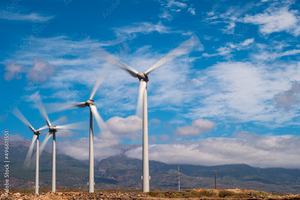 group of windmills lined up on the left with blades in motion. blue sky with clouds. group of windmills lined up on the left with blades in motion. blue sky with clouds.