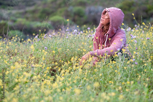 woman looking at the sky at dawn green and flowery meadow in spring, pink sweater with hoodie