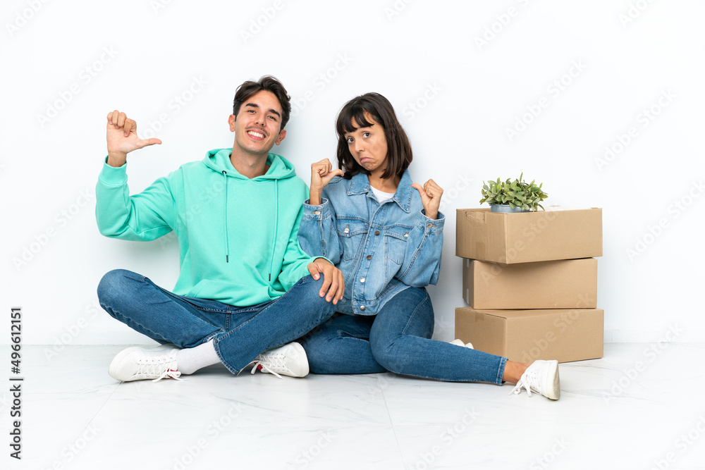 Young couple making a move while picking up a box full of things sitting on the floor isolated on white background proud and self-satisfied in love yourself concept Young couple making a move while picking up a box full of things sitting on the floor isolated on white background proud and self-satisfied in love yourself concept