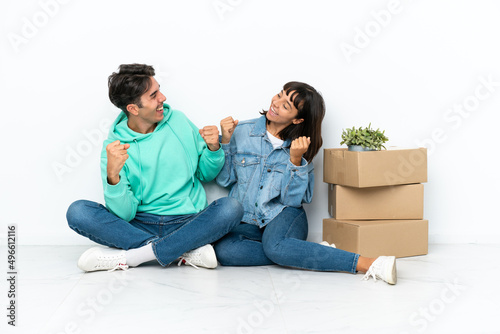 Young couple making a move while picking up a box full of things sitting on the floor isolated on white background celebrating a victory in winner position © luismolinero