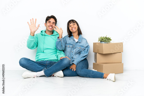 Young couple making a move while picking up a box full of things sitting on the floor isolated on white background saluting with hand with happy expression © luismolinero