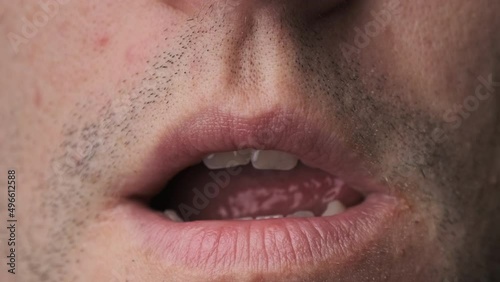 Man erotically licks his lips close-up. Close-up portrait of the face of a young man with stubble who is sexually licking his lips with his tongue. Macro of seductive young man. Sexually horny concept photo