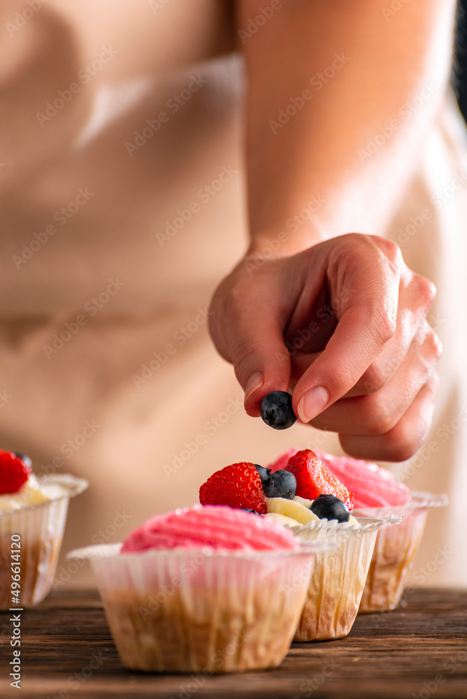 Pastry chef decorates the muffins with fresh berries. Cupcakes with strawberries and blueberries. Vertical frame. Close up.