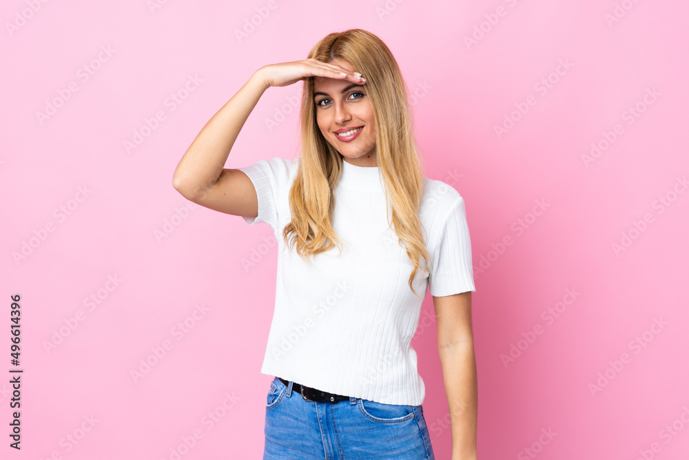 Young Uruguayan blonde woman over isolated pink background looking far away with hand to look something Young Uruguayan blonde woman over isolated pink background looking far away with hand to look something