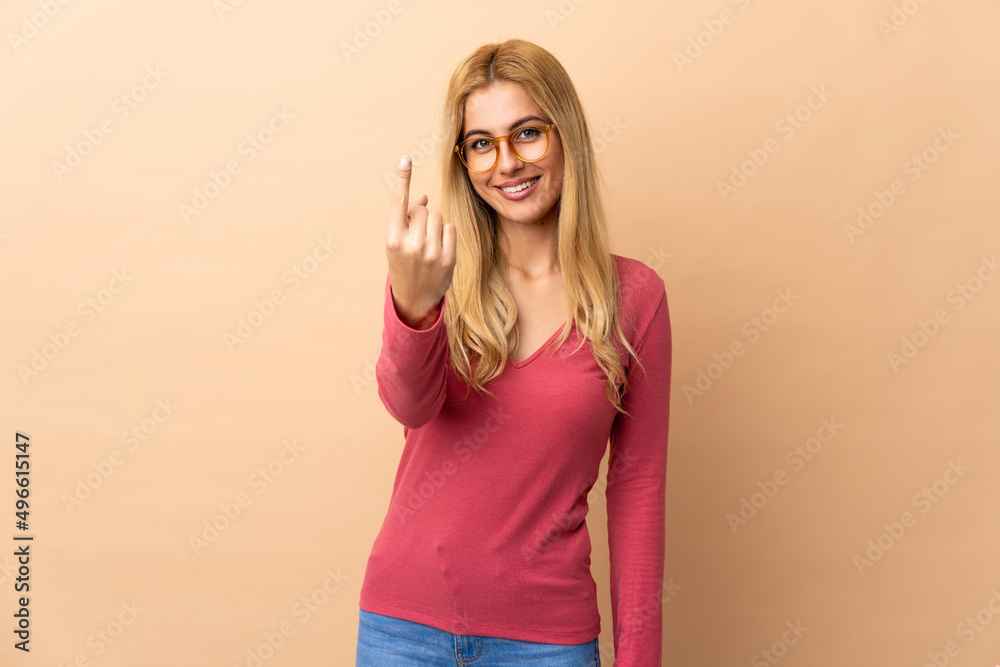 Young Uruguayan blonde woman over isolated background doing coming gesture Young Uruguayan blonde woman over isolated background doing coming gesture