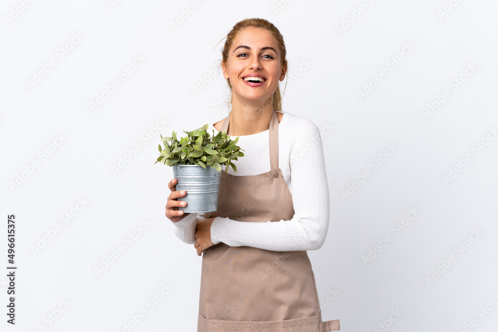 Young blonde gardener woman girl holding a plant over isolated white background laughing Young blonde gardener woman girl holding a plant over isolated white background laughing